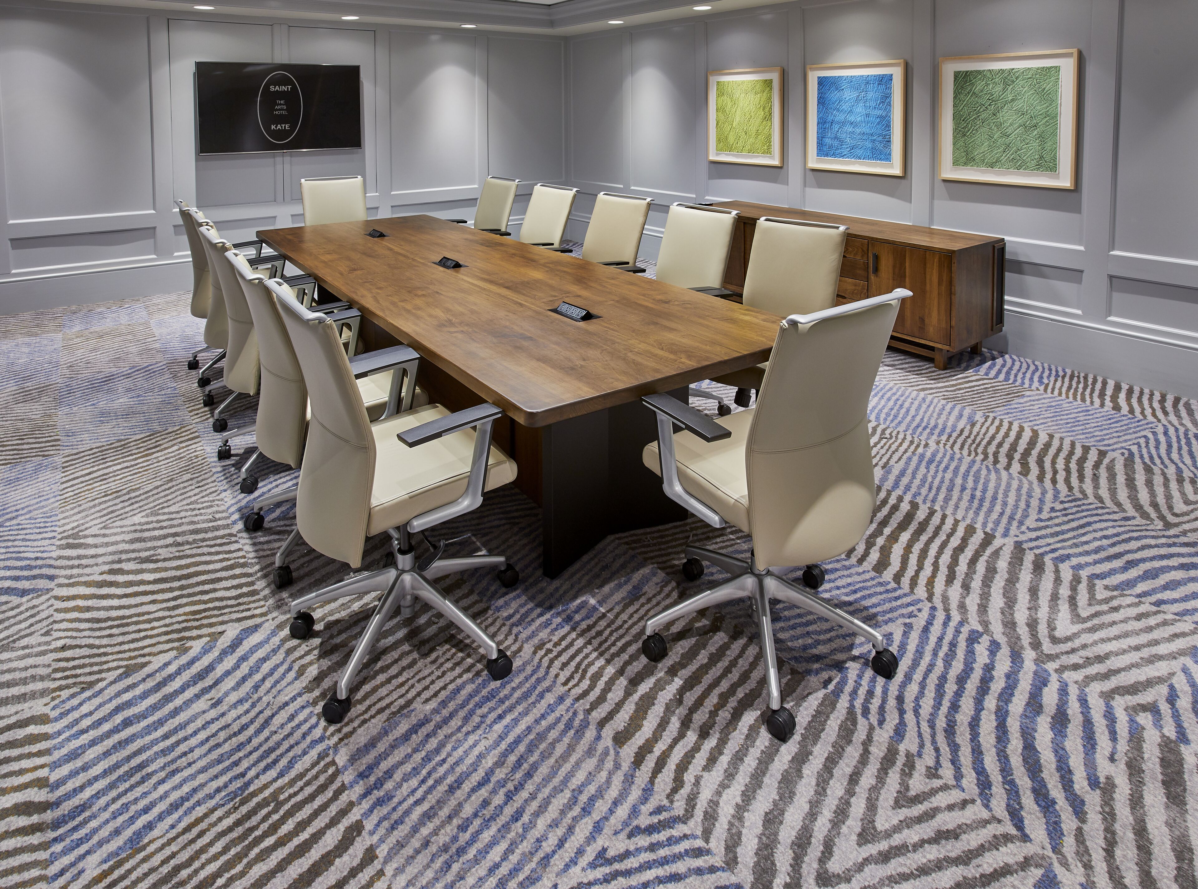 A conference room with a long table, multiple chairs, a TV on the wall, and framed artwork.