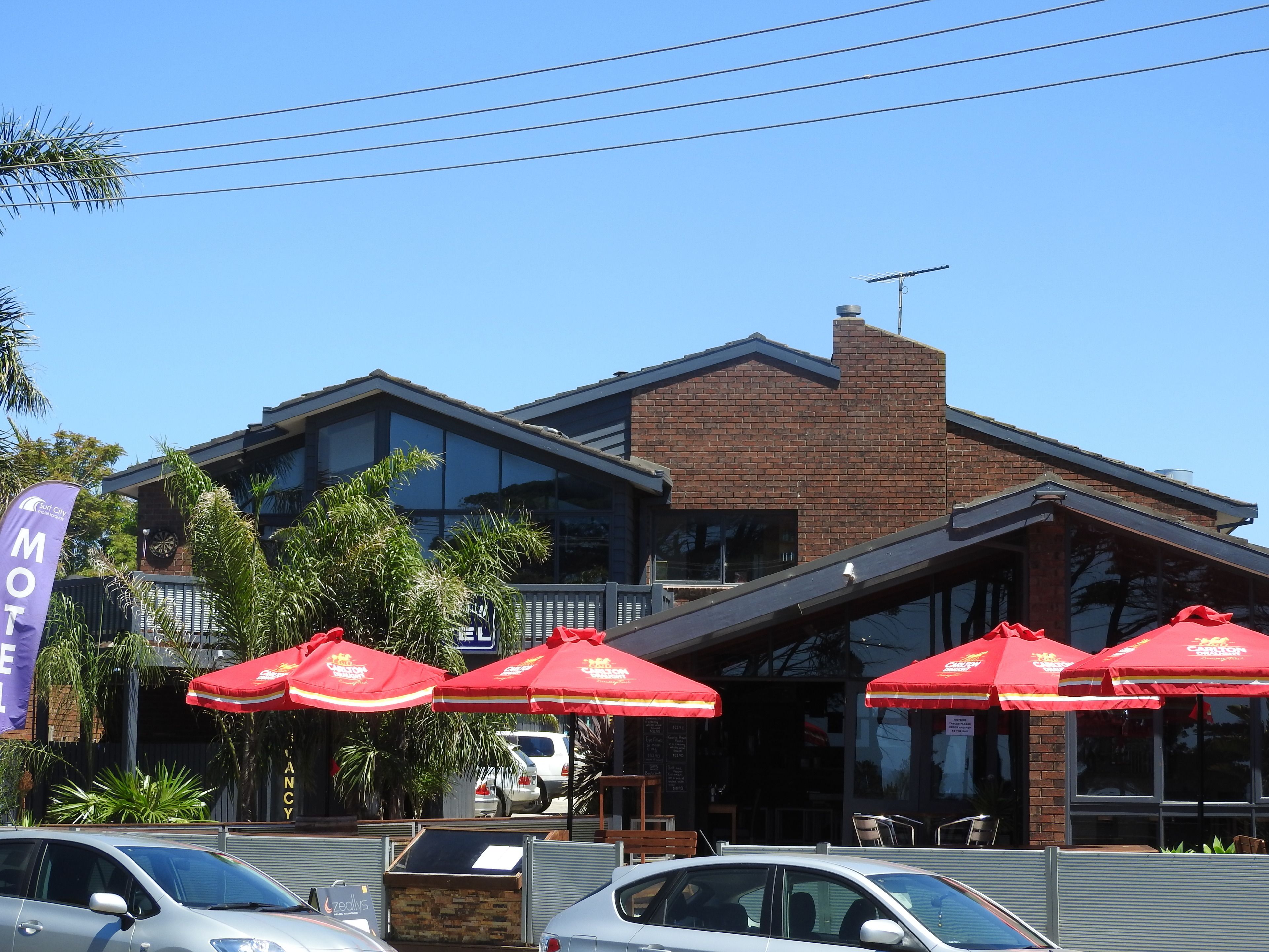 A motel with a brick facade, large windows, and red umbrellas.
