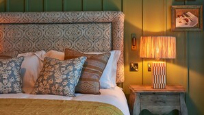 A bed with patterned pillows, a bedside lamp, and a wooden nightstand with a drawer. - The White Horse - A Heartwood Inn (Dorking)