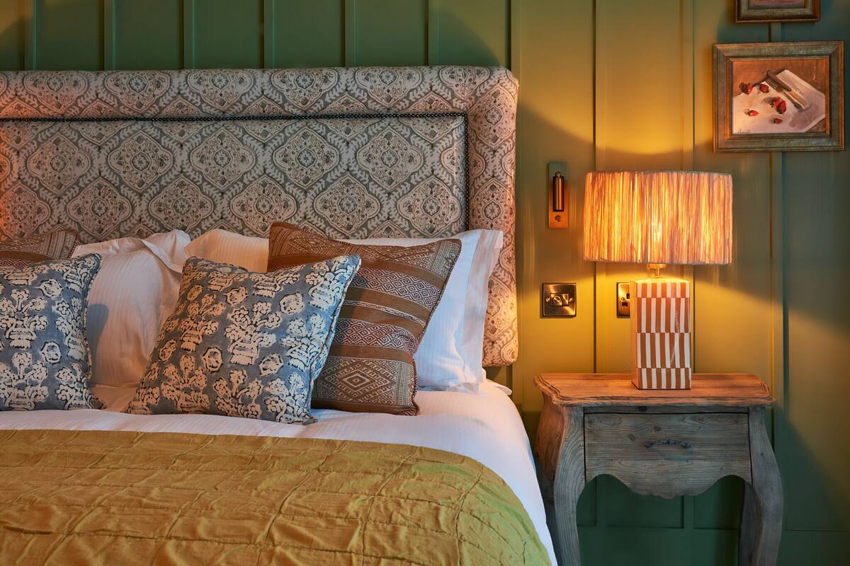 A bed with patterned pillows, a bedside lamp, and a wooden nightstand with a drawer.