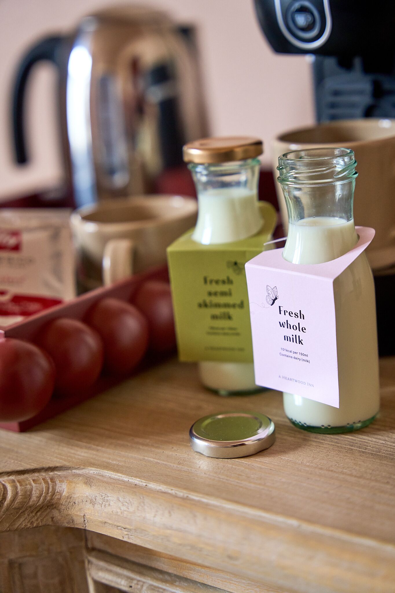 Une table en bois sur laquelle se trouvent une bouteille de lait frais entier, une boîte d’œufs et une machine à café.