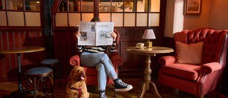 Una habitación acogedora con una persona leyendo el periódico, un perro y un sillón rojo.