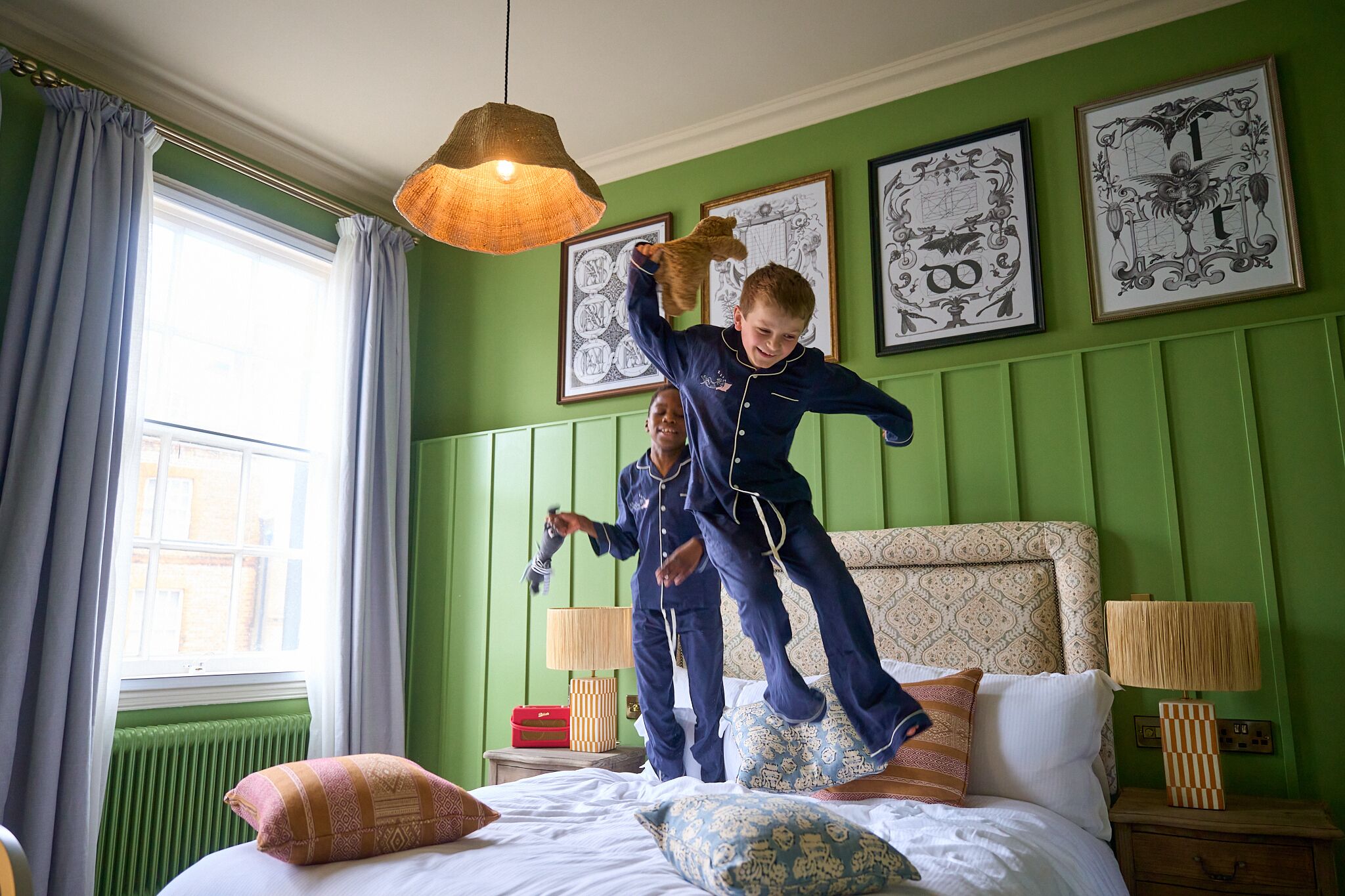Une pièce aux murs verts, un lit agrémenté d’oreillers à motifs, une fenêtre avec des rideaux et des œuvres d’art encadrées accrochées au mur.