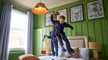 Une pièce aux murs verts, un lit agrémenté d’oreillers à motifs, une fenêtre avec des rideaux et des œuvres d’art encadrées accrochées au mur.