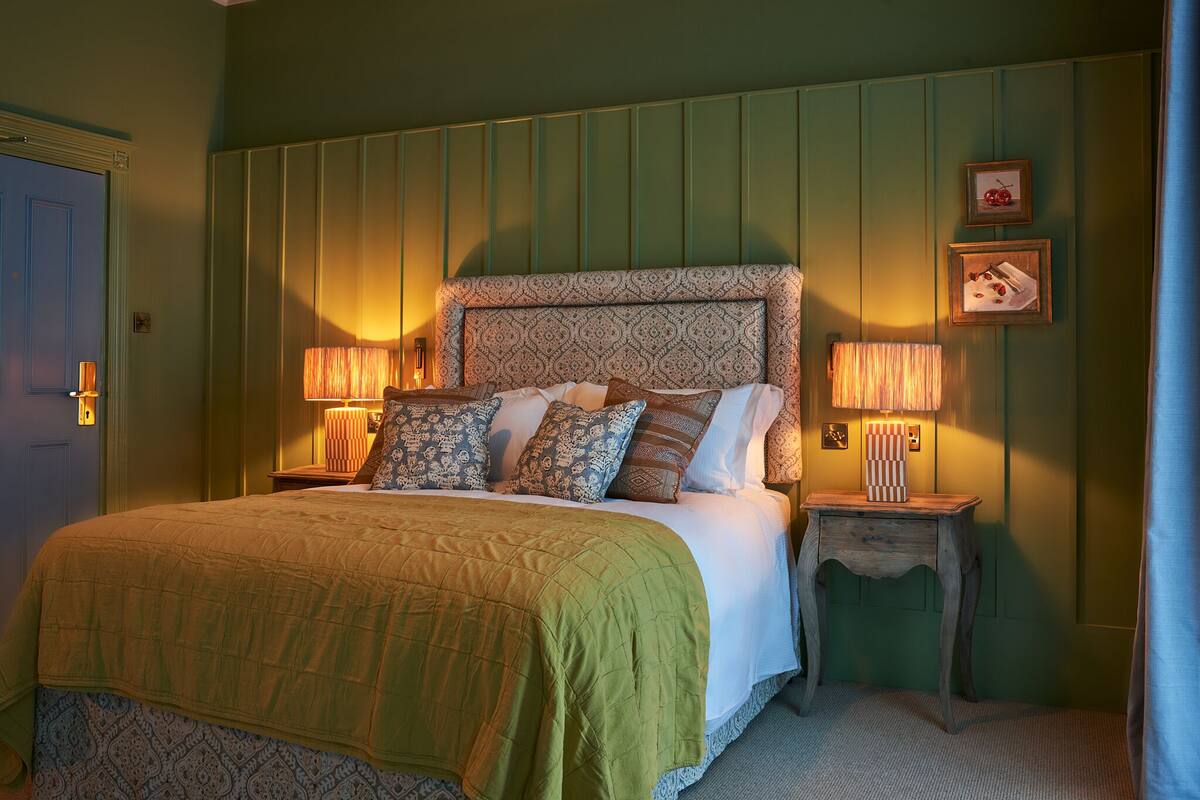 A neatly made bed with a patterned headboard, two bedside lamps, and a small wooden nightstand.