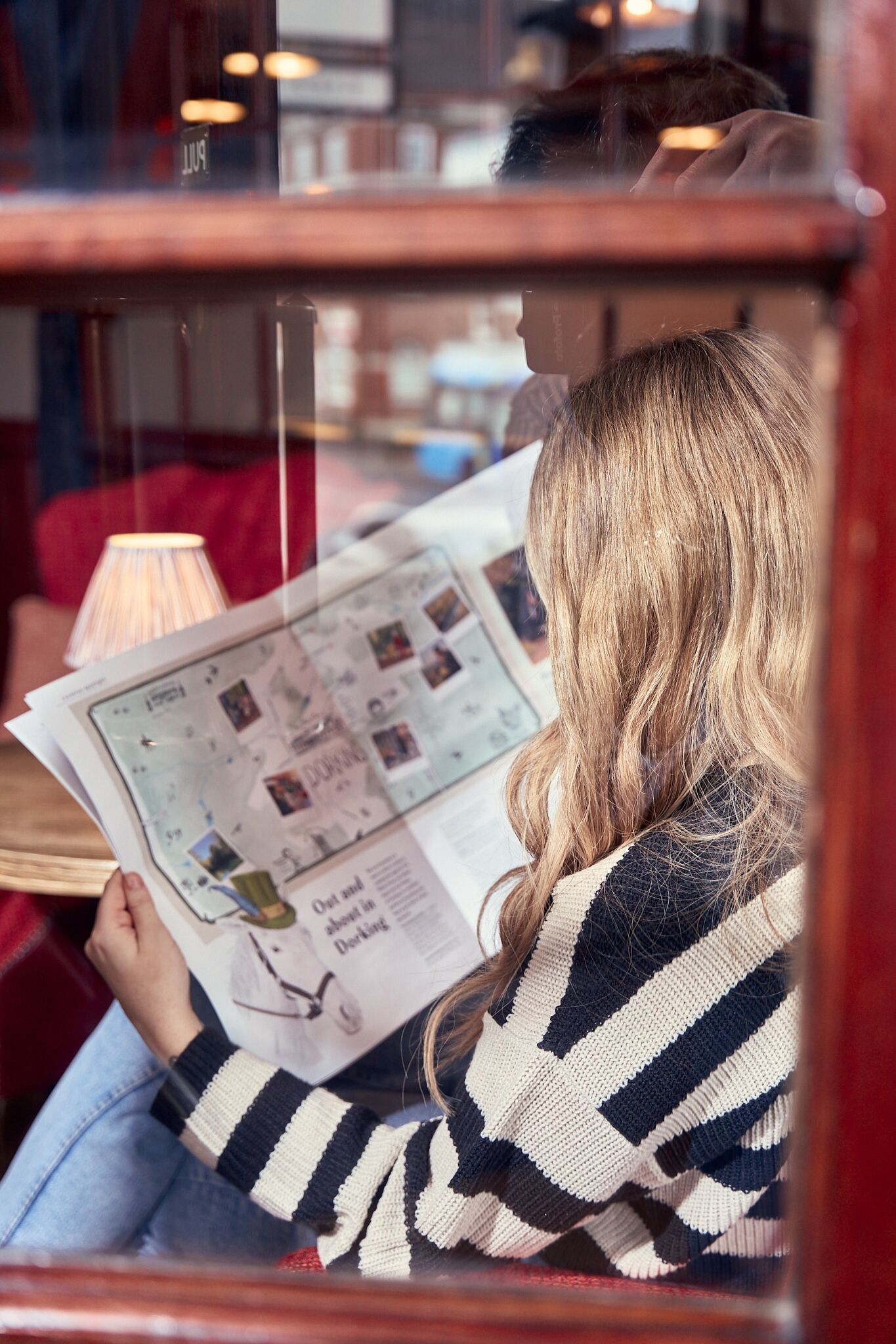 A person reading a newspaper at a table with a lamp.