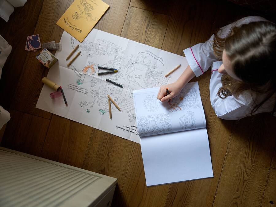 Uma pessoa sentada à mesa de madeira com um livro grande aberto e diversas ferramentas de desenho.