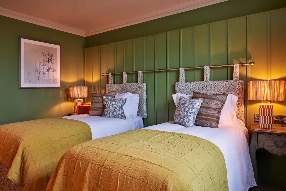 A double room with two beds, green walls, patterned headboards, and bedside lamps.