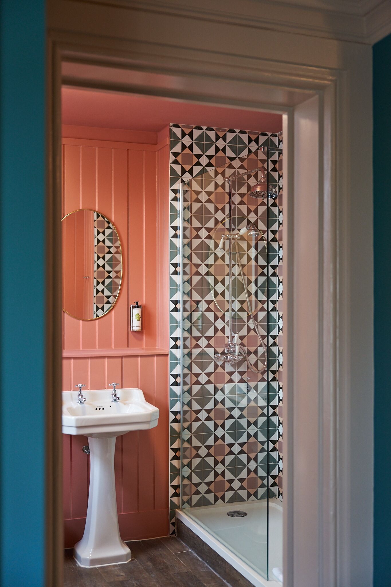 Une salle de bain avec un lavabo sur colonne, un miroir et une douche dont les carreaux présentent un motif géométrique.