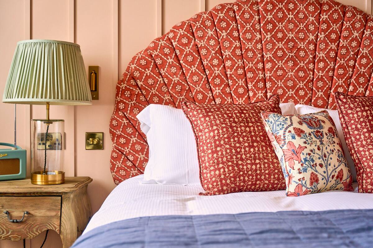 A bed with a red patterned headboard, a green lamp, and a wooden nightstand with a radio.