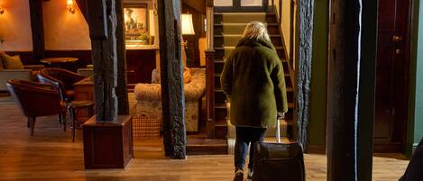 A person walking through a lobby with wooden floors, a staircase, and a seating area with chairs and a sofa.