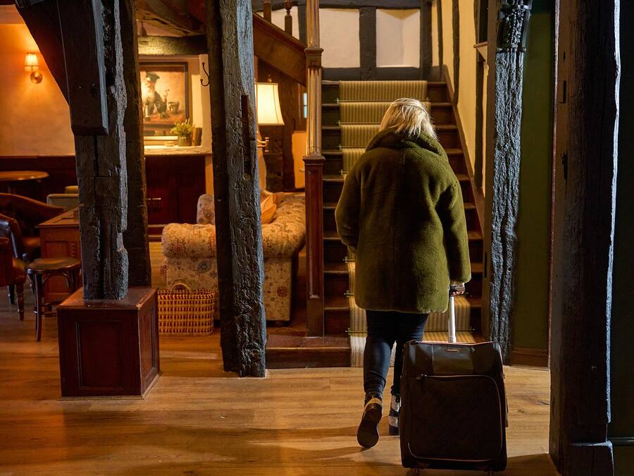 A person walking through a lobby with wooden floors, a staircase, and a seating area with chairs and a sofa.