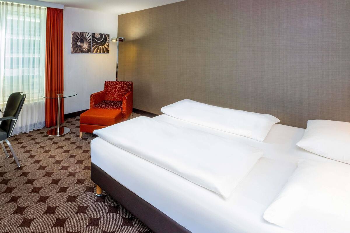 Ein Hotelzimmer mit einem großen Bett, einem Sessel, einem Tisch und einem Fenster mit Vorhängen.