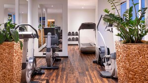 A gym with exercise equipment, wooden flooring, and potted plants.