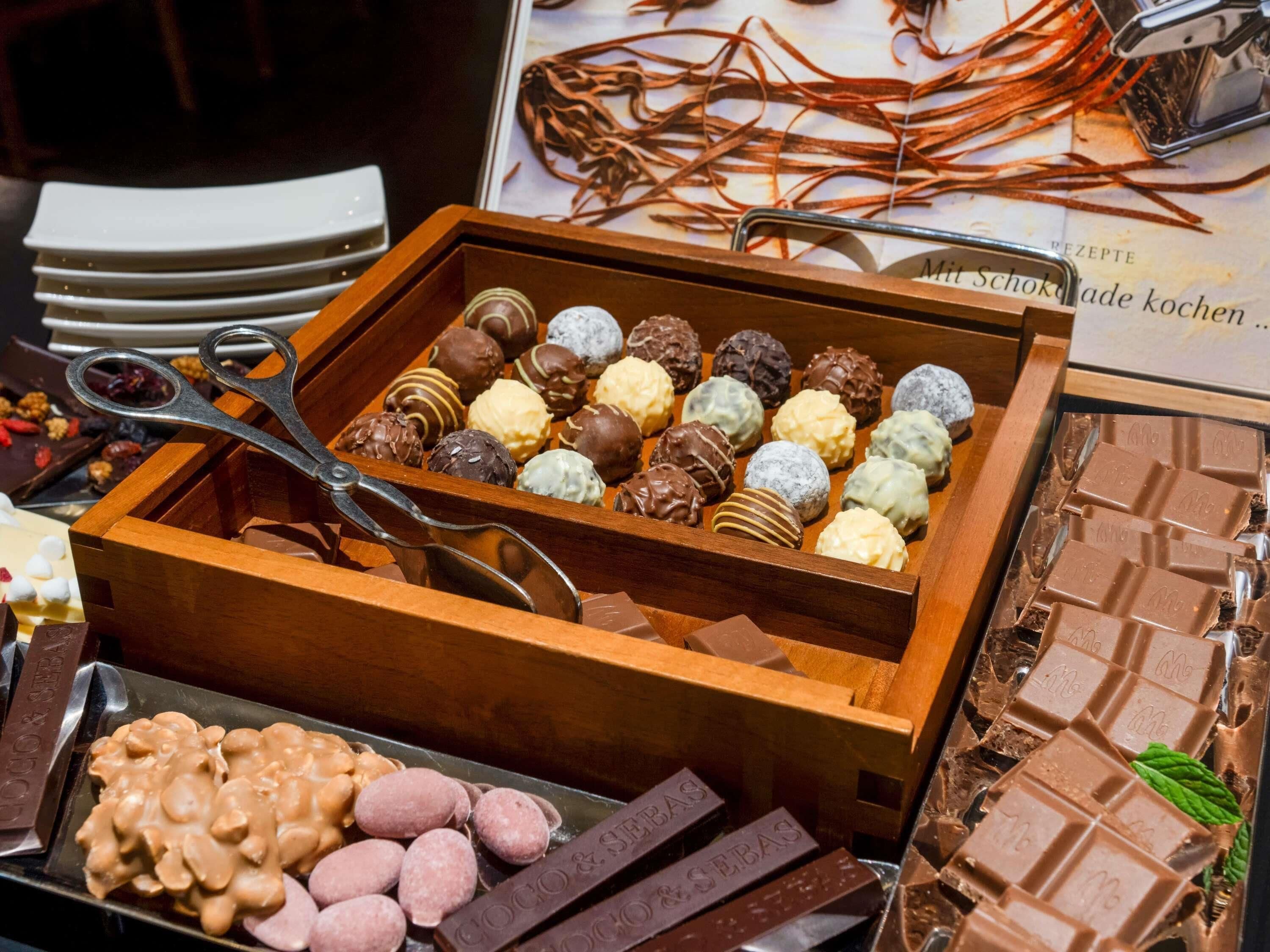 A variety of chocolates and desserts in a wooden box, with a pair of scissors on top.