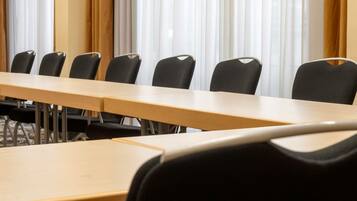 A conference room with a long table and chairs, large windows with curtains, and a carpeted floor.