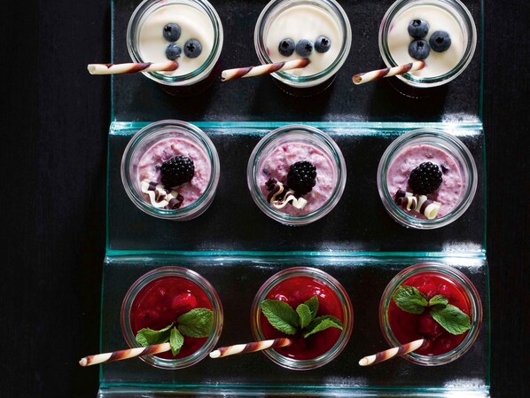 Six pots en verre contenant différents desserts à base de fruits rouges, chacun accompagné d’une paille.