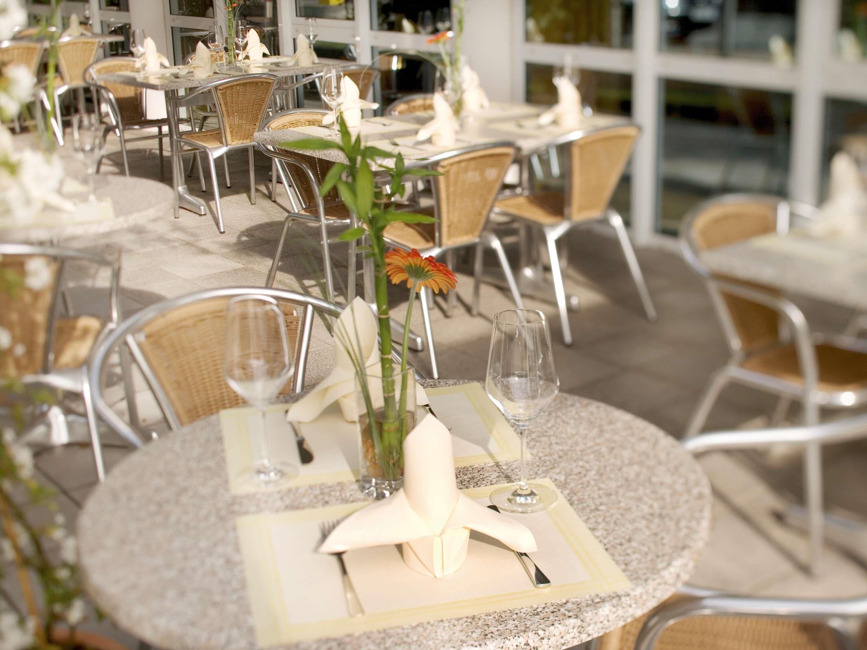 Ein Restaurant mit runden Tischen, Korbstühlen und einer Glasvase mit Blumen.