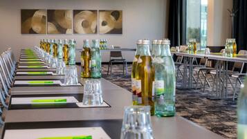 Un salón de conferencias con mesas largas, botellas de vidrio y marcadores verdes.