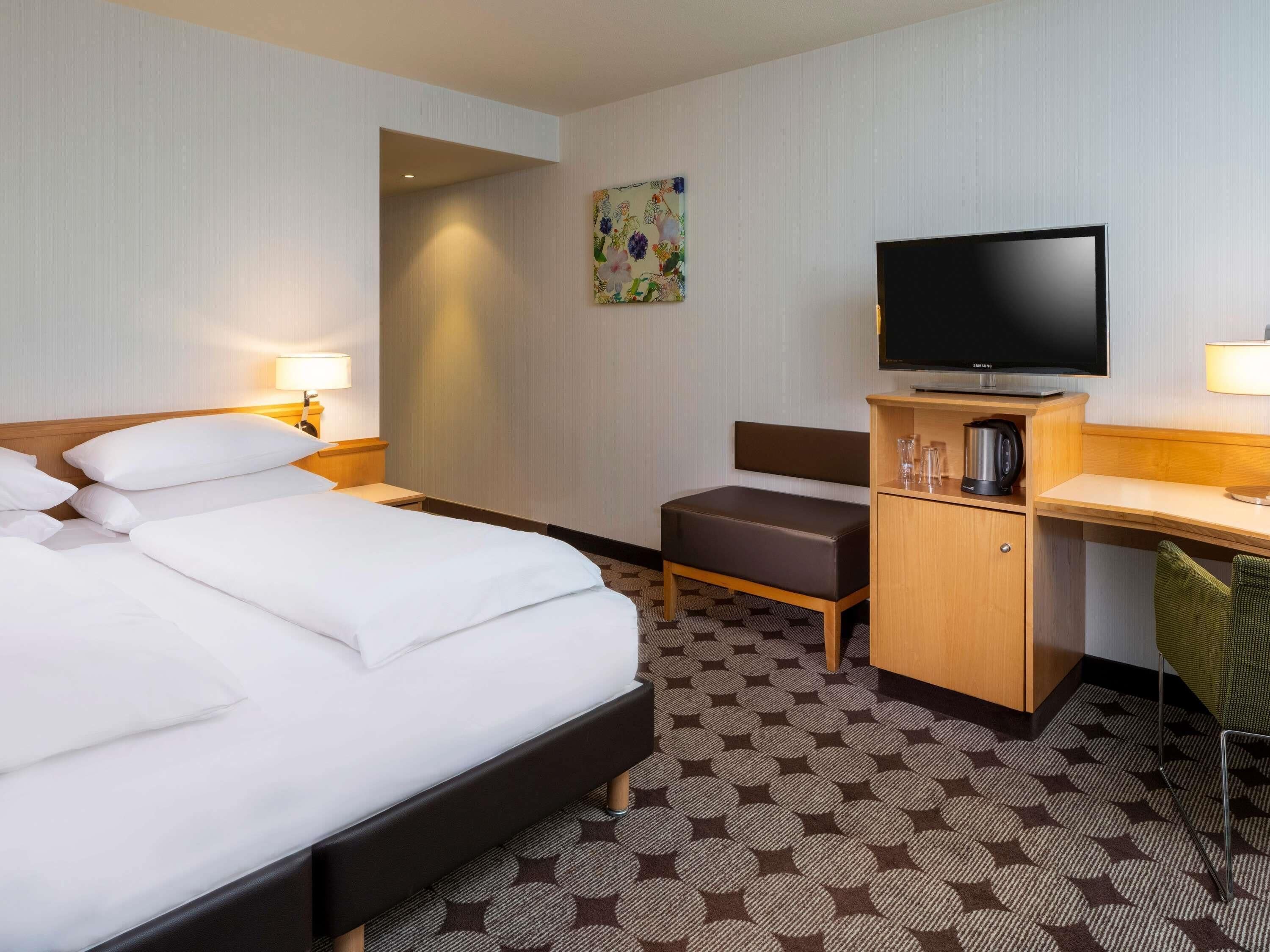 Una habitación de hotel con una cama grande, un escritorio, un televisor y un pequeño rincón de descanso.