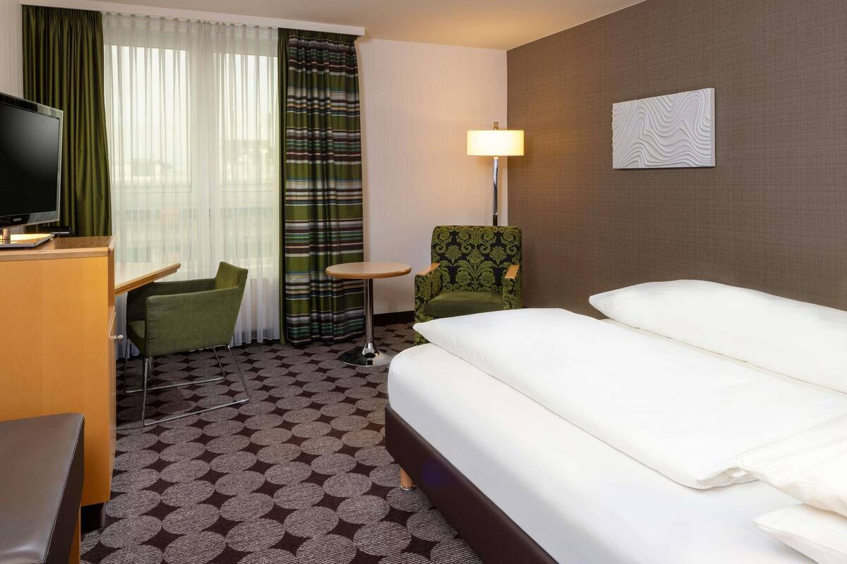 Ein Hotelzimmer mit Bett, Schreibtisch mit Fernseher, Stuhl, kleinem Tisch und Lampe.