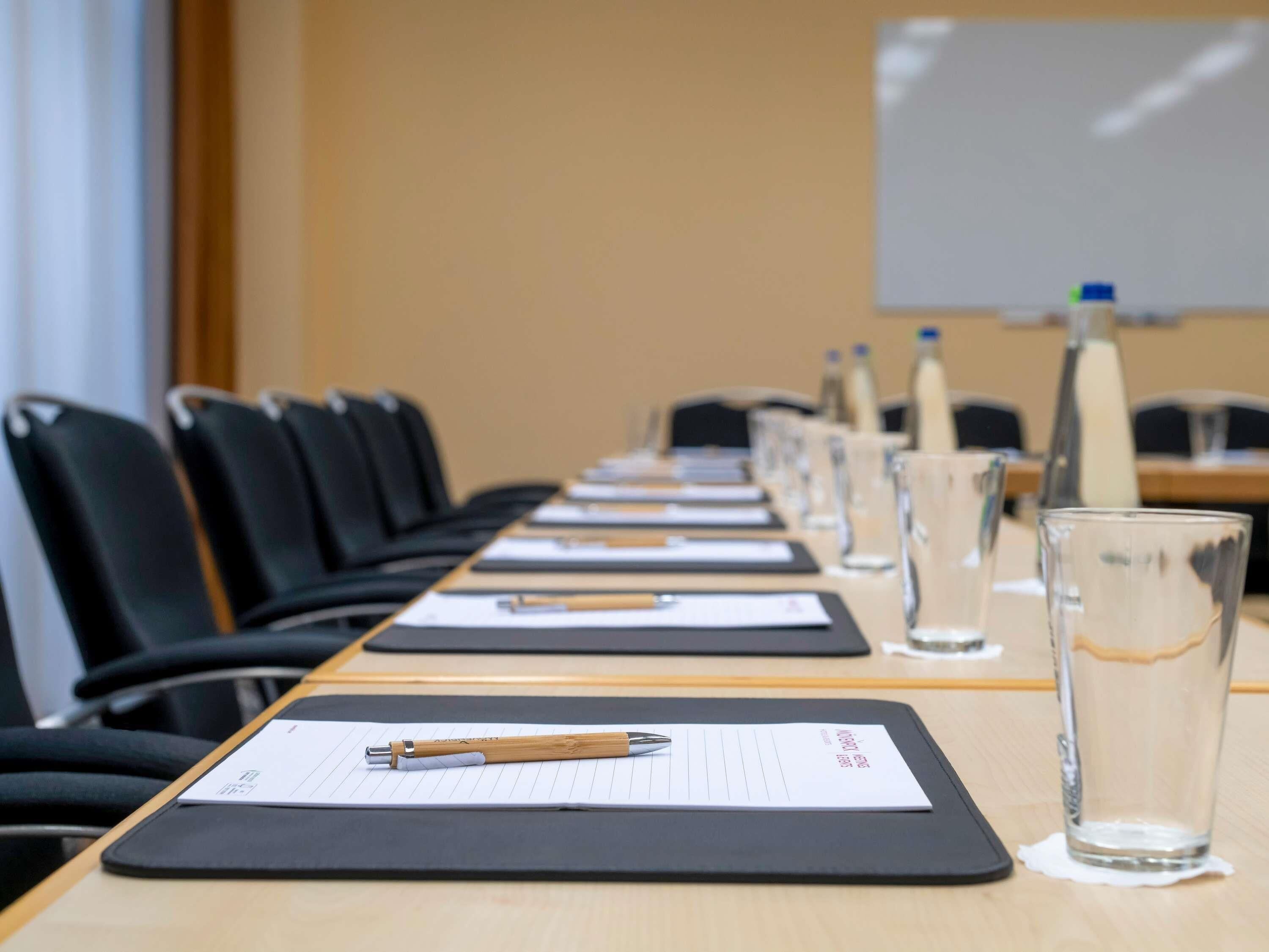 Ein Konferenzraum mit einem langen Tisch, Stühlen, Wasserflaschen und einer Whiteboard-Tafel.