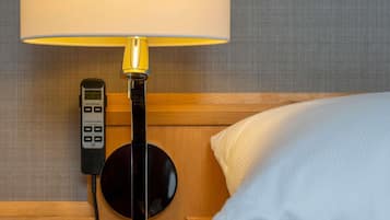 A bed with a white pillow, a bedside lamp, and a control panel on the wall.