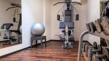 A gym with exercise equipment, a mirrored wall, and a wooden floor.