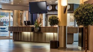 A hotel reception area with a reception desk, a flat-screen TV, clocks, and potted plants.