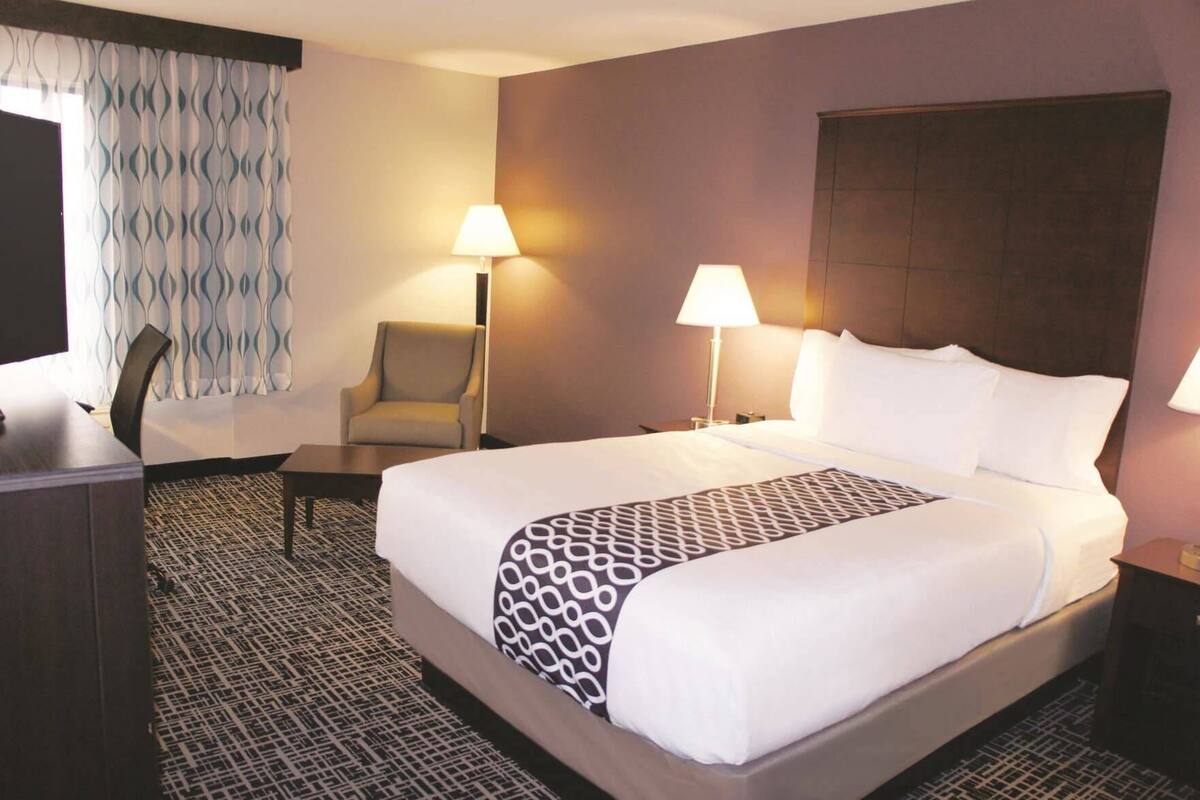 A hotel room with a large bed, two bedside lamps, a chair, a desk, and a patterned rug.