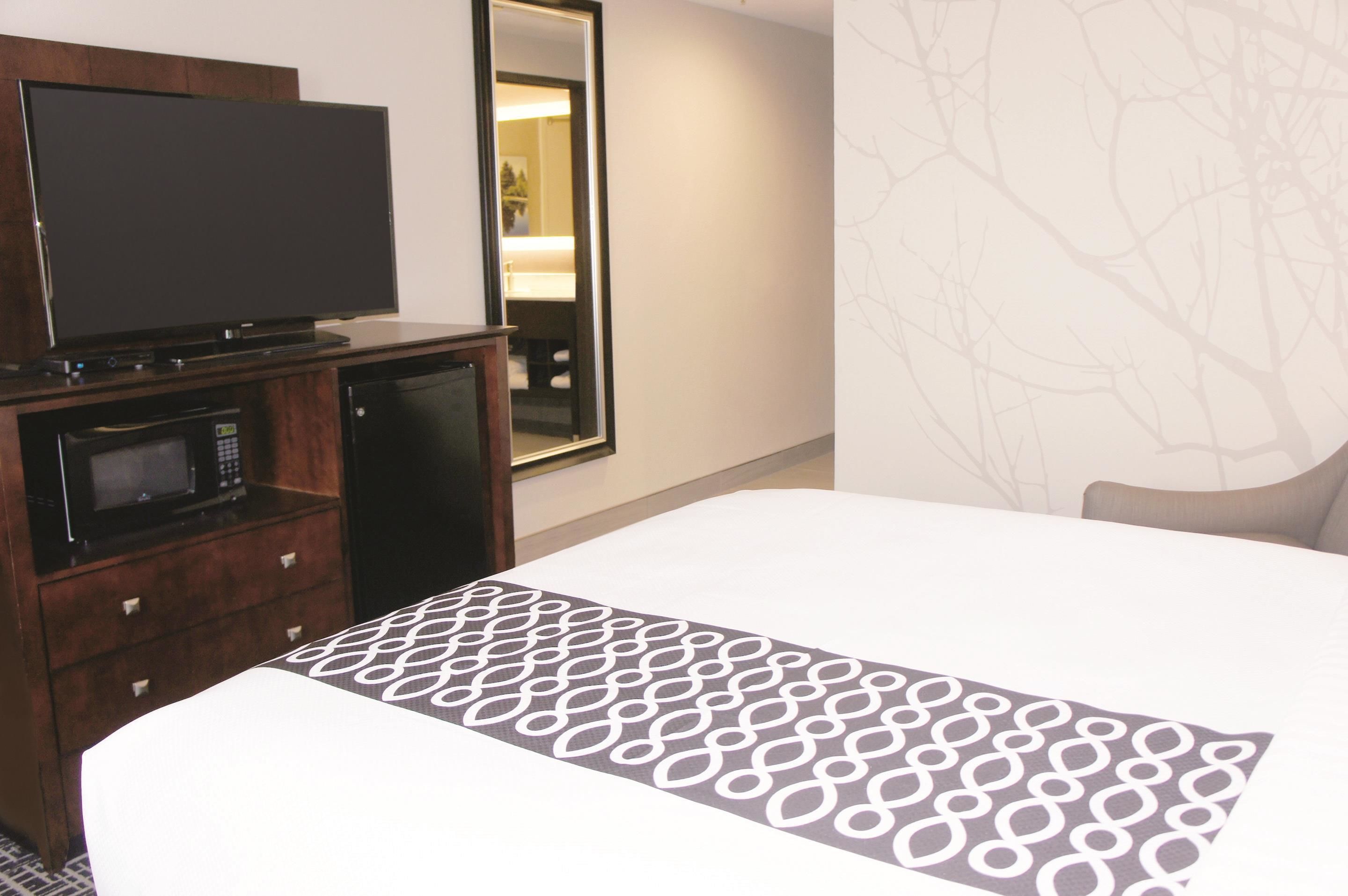 Habitación de hotel con una cama, un televisor sobre un mueble de madera, un microondas y un espejo.