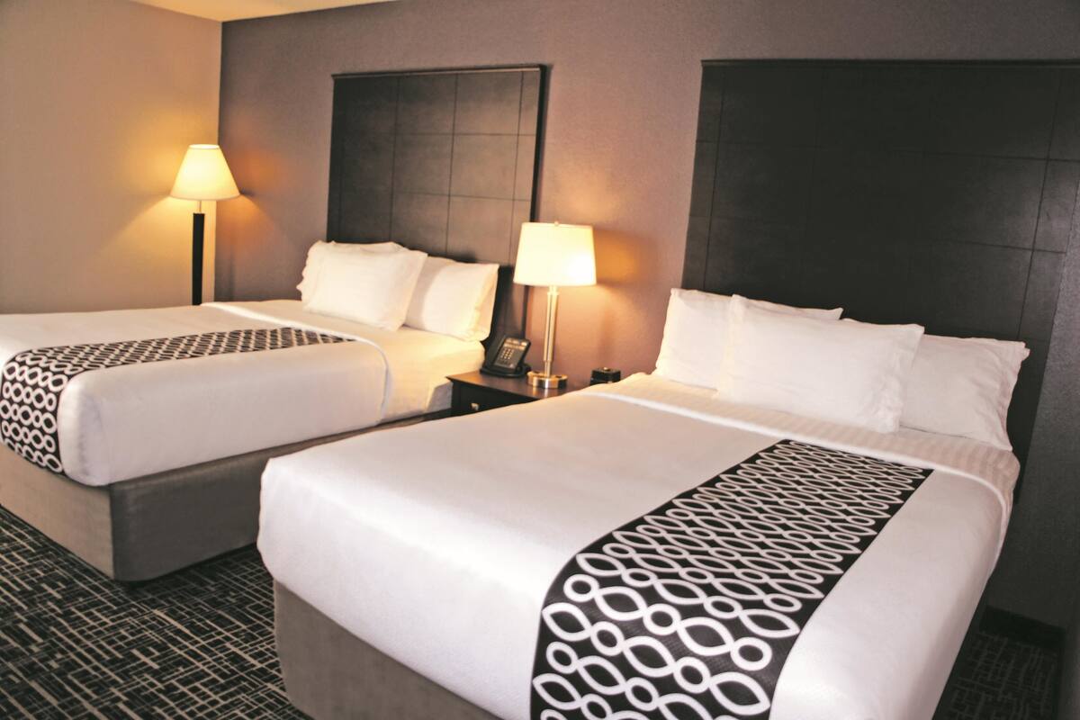 A hotel room with two beds, each with a patterned bedspread, bedside lamps, and a dark headboard.