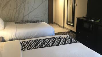 Quarto de hotel com duas camas, um espelho grande, uma televisão e uma cômoda.