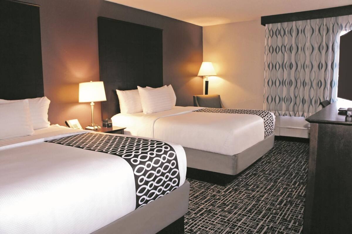 A hotel room with two beds, a desk, a chair, a lamp, and a patterned curtain.