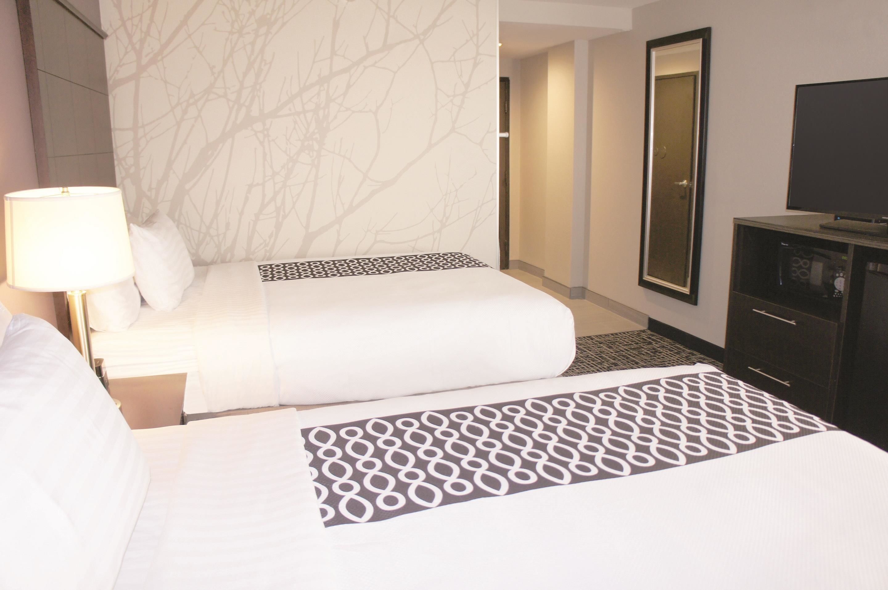 A hotel room with two beds, a large mirror, a TV, and a patterned rug.