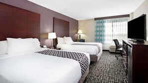 Habitación de hotel con dos camas, televisor, escritorio y alfombra estampada.