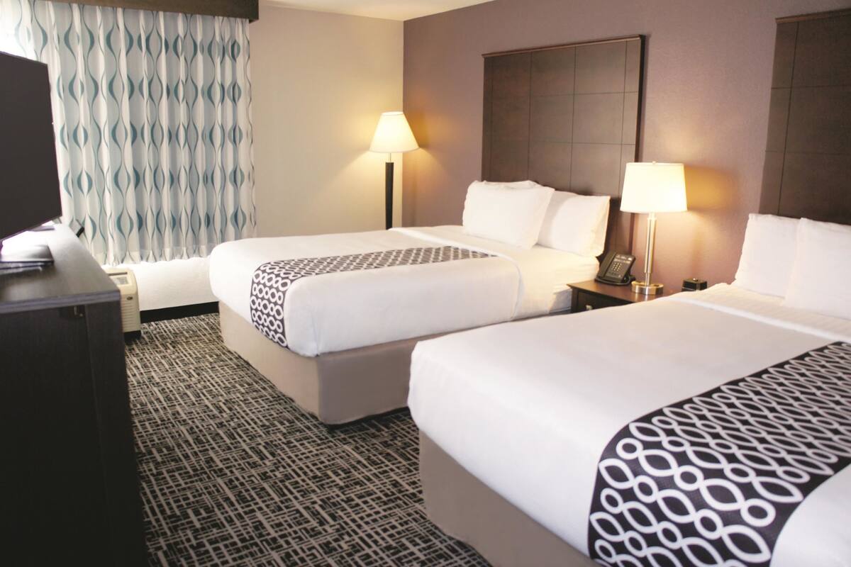 A hotel room with two beds, a desk, a TV, and a patterned carpet.