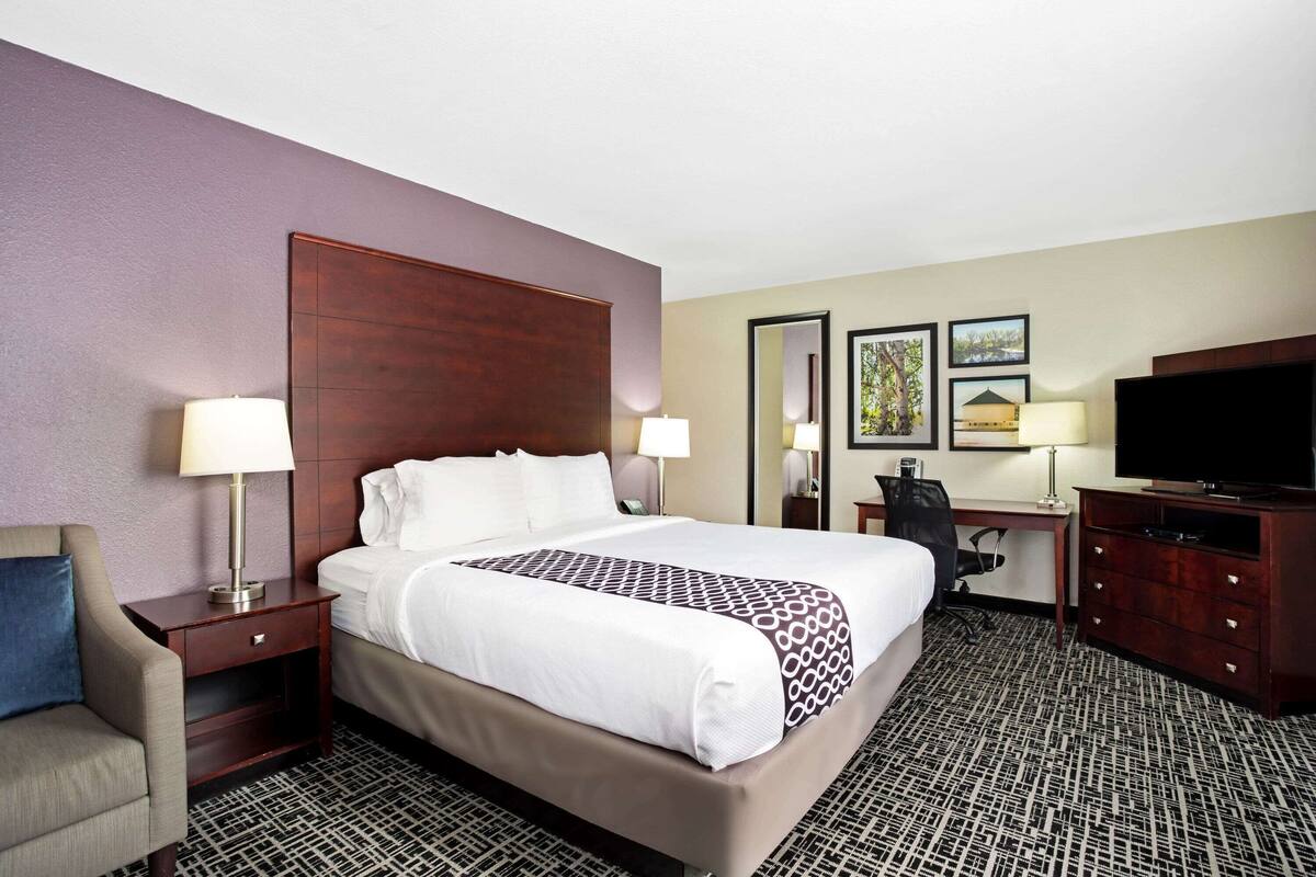A hotel room with a large bed, two bedside tables, a desk with a chair, a television, and artwork on the wall.