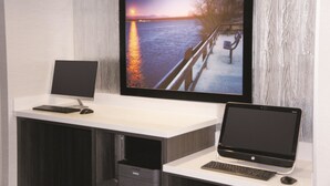 Un espacio de trabajo moderno con una televisión de pantalla plana grande montada en la pared, una computadora de escritorio y una laptop sobre un escritorio.
