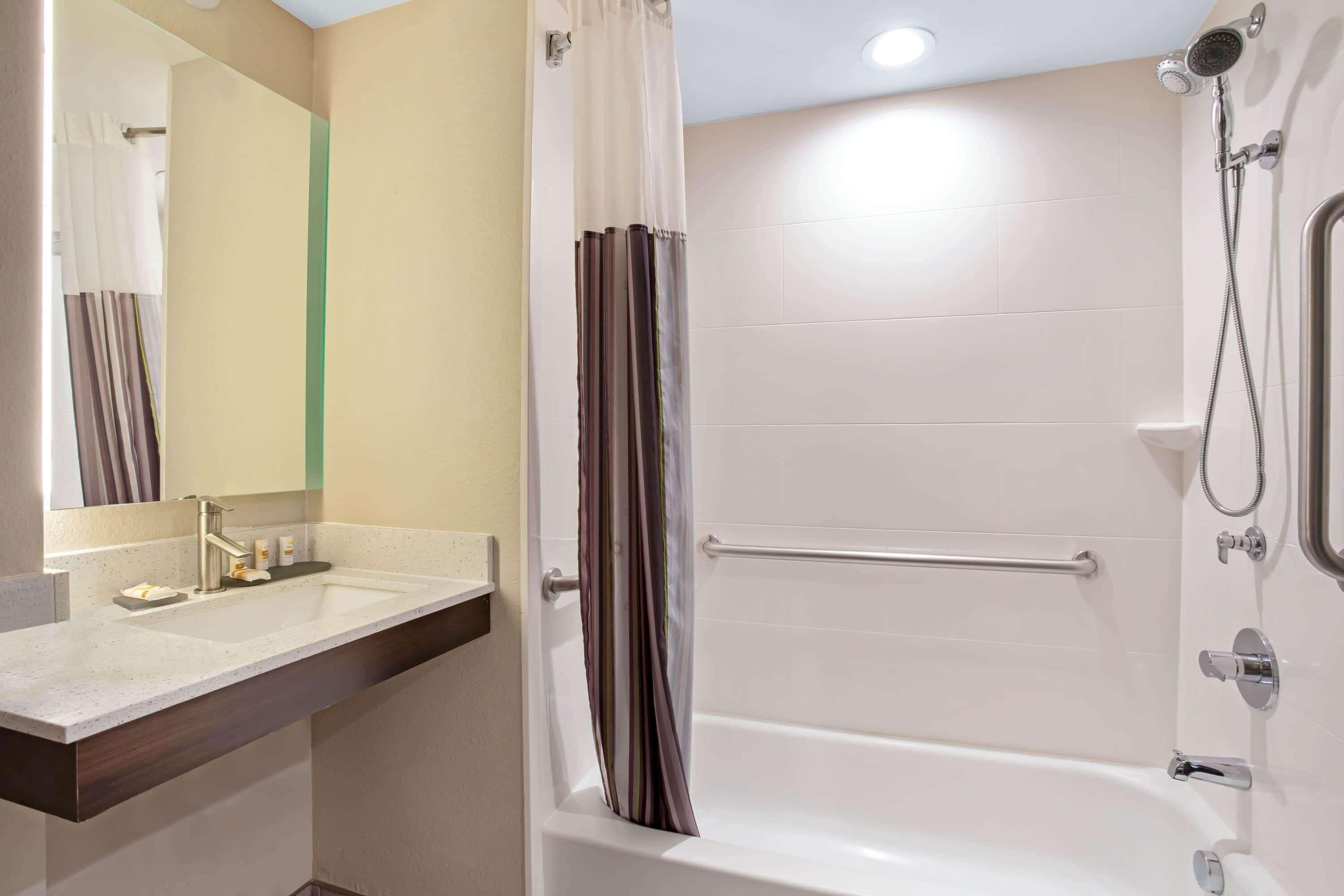 A bathroom with a sink, mirror, shower, and grab bar.