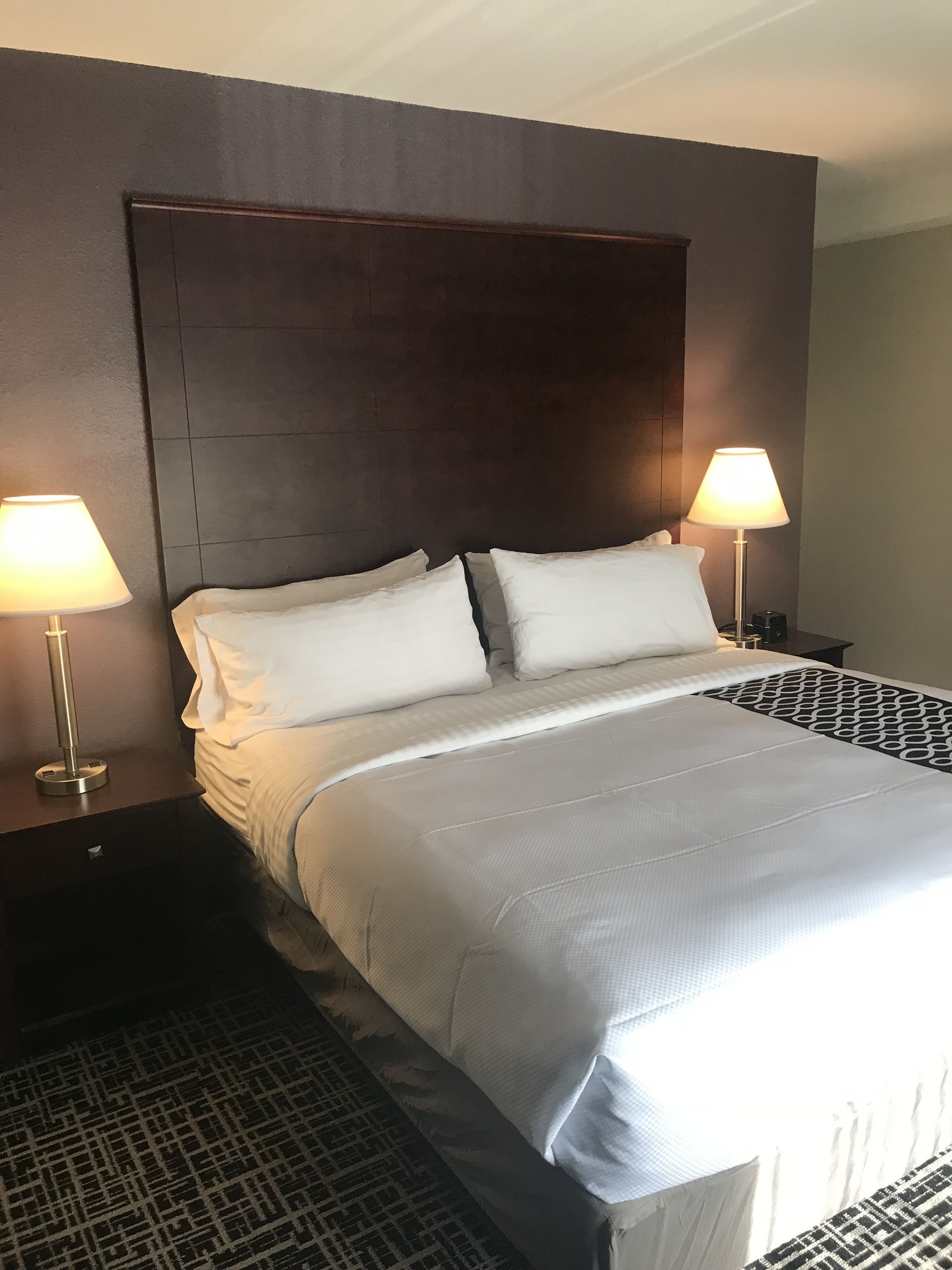 Hotellihuone, jossa on suuri sänky, kaksi yöpöytävalaisinta ja tumma pääty.