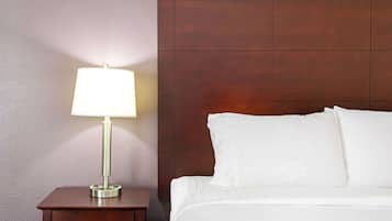 A neatly made bed with white linens and pillows, a bedside table with a lamp, and a wooden headboard.