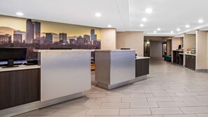 Zona de recepción de hotel con un mural de paisaje urbano, varias mesas de recepción y piso de baldosas.