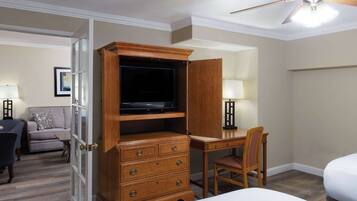 A hotel room with a wooden desk, a television, a chair, a bed, and a ceiling fan.