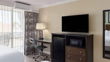 Una habitación de hotel con cama, escritorio con silla, televisor, microondas y un ventanal con cortinas.