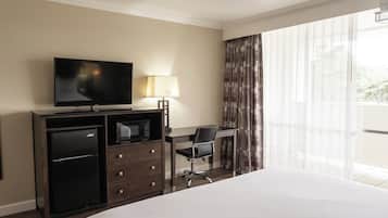 A hotel room with a bed, a desk, a television, a refrigerator, and a lamp.