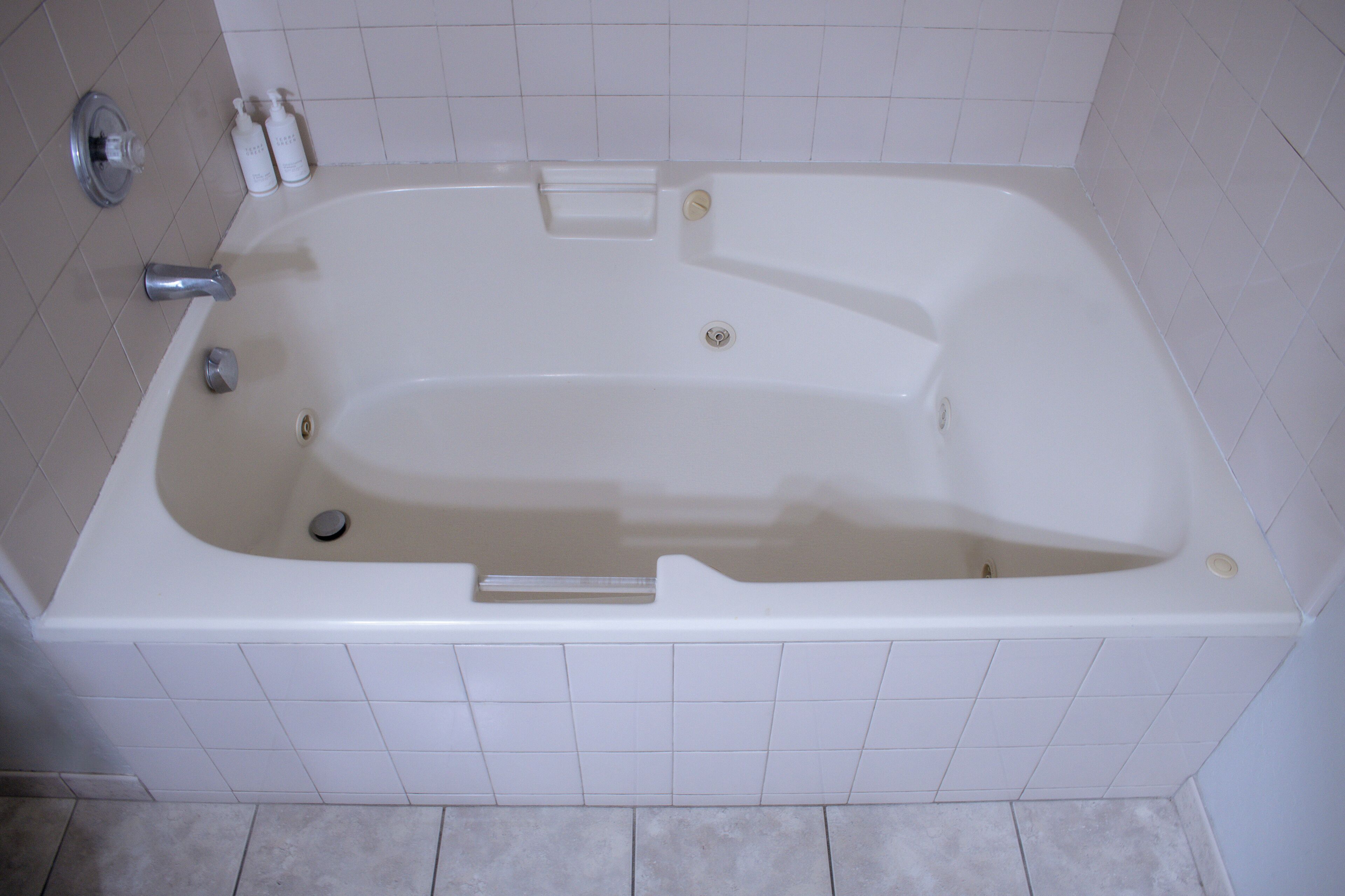 A white bathtub with a built-in seat, a handheld showerhead, and a drain.