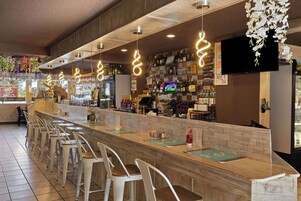 Una zona de bar con una barra larga, varios taburetes y una pantalla de televisión en la pared.