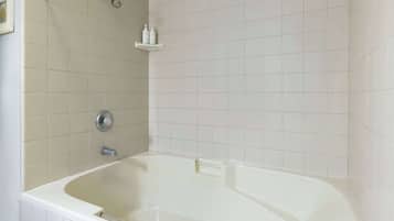 Un baño con bañera, ducha y estante con artículos de aseo.