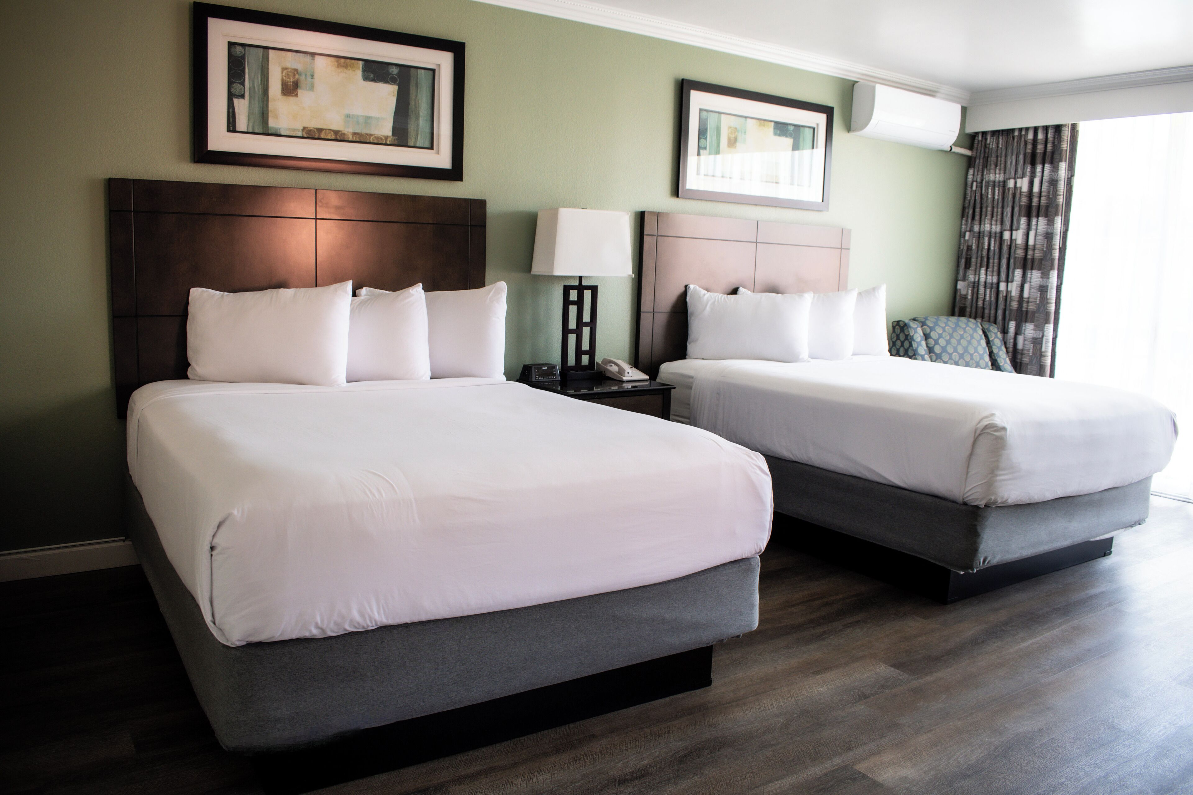 Two adjacent beds with headboards, a bedside table with a lamp, and framed artwork on the walls.